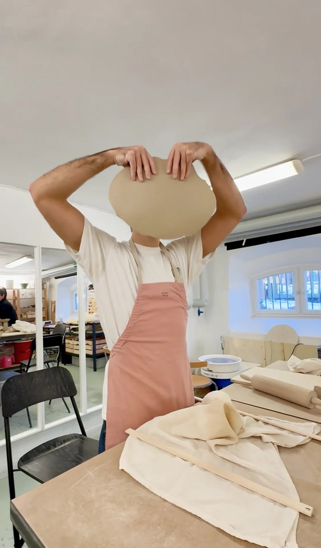 Person in a pink apron holding up a freshly shaped clay plate